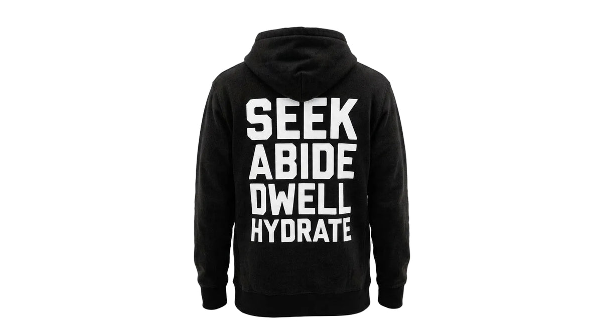 A black pullover hoodie shown from the back, featuring the words 'SEEK ABIDE DWELL HYDRATE' printed in large white capital letters on the back, set against a plain white background.