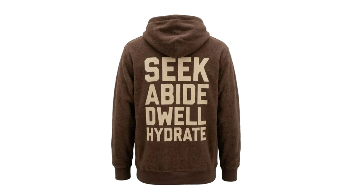 A brown pullover hoodie shown from the back, featuring the words 'SEEK ABIDE DWELL HYDRATE' printed in large beige block letters.